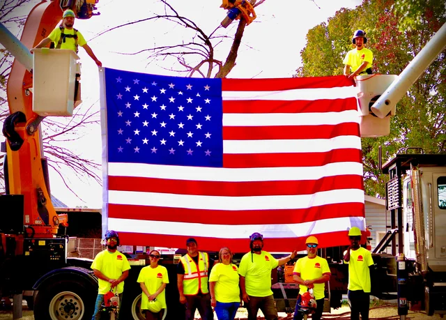 Tree Wizard crew holding an American flag between two bucket trucks in Columbia, MO