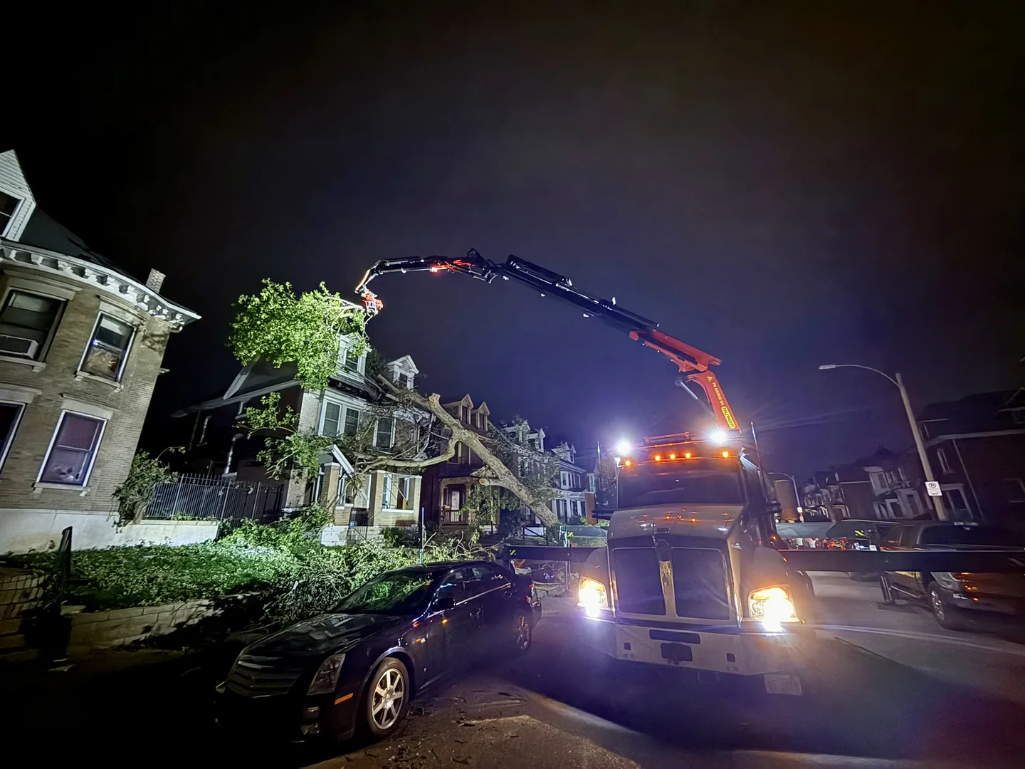 Crane removing an emergency tree from a roof at night